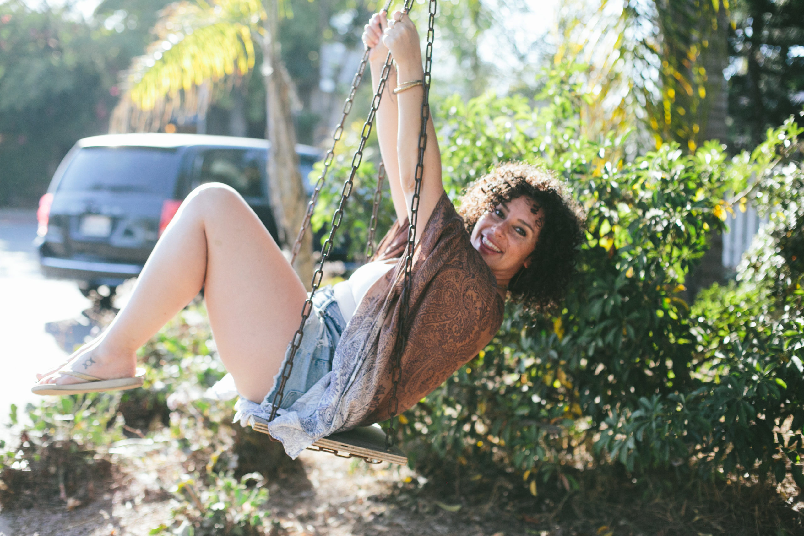 Elizabeth swinging in front of large plant wearing shorts